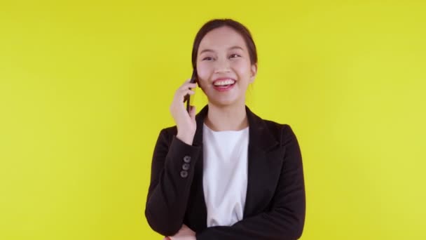 Joven mujer de negocios asiática en traje hablando en el teléfono inteligente aislado en el fondo amarillo, mujer de negocios hablando en el teléfono inteligente con conversación, mujer sosteniendo el teléfono celular, concepto de comunicación. - Imágenes, Vídeo