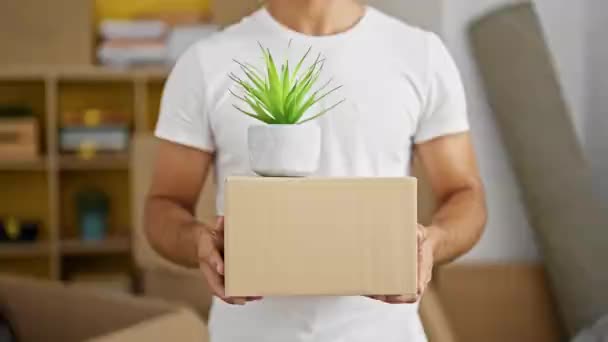 Mladý hispánec se usmívá sebevědomě drží balíček a květináč v novém domově - Záběry, video