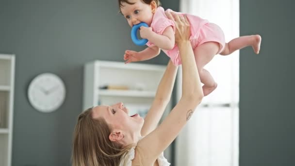 Madre e hija abrazándose mutuamente sosteniendo al bebé en el aire en casa - Imágenes, Vídeo