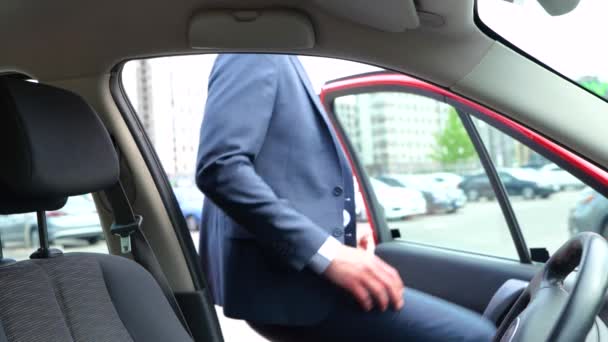 Nuori tyylikäs pukumies avaamassa ovea ja astumassa autoon. Mies käyttää turvavyötä. Liikenne, liiketoiminta, turvallisuus ja ihmisten käsite. Hidastus - Materiaali, video