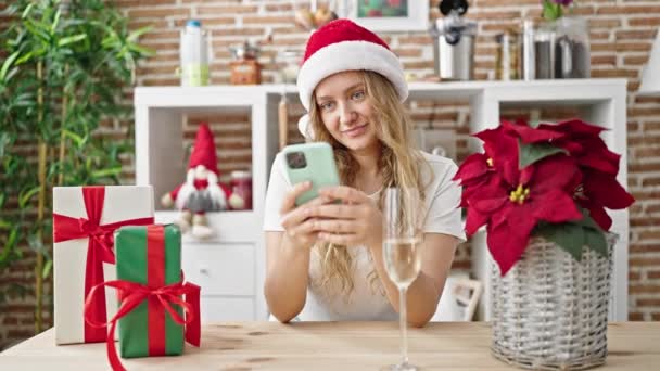 Νεαρή ξανθιά γυναίκα γιορτάζει τα Χριστούγεννα χρησιμοποιώντας smartphone πίνοντας σαμπάνια στην τραπεζαρία - Πλάνα, βίντεο