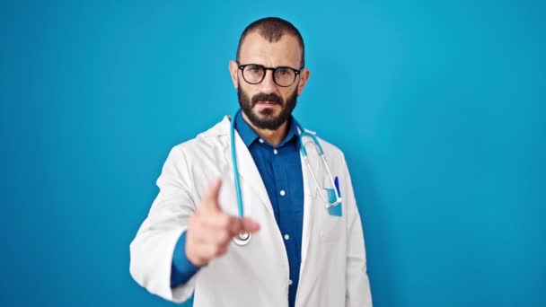Junger hispanischer Arzt zeigt wütend mit dem Finger auf isolierten blauen Hintergrund - Filmmaterial, Video