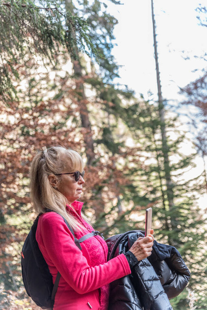 Érett nő fényképez a természeti táj a mobiltelefon, miközben felfedezi az erdőben. Technológia és utazási koncepció. - Fotó, kép