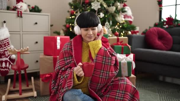 Jeune femme chinoise écoutant de la musique boire du café par arbre de Noël à la maison - Séquence, vidéo