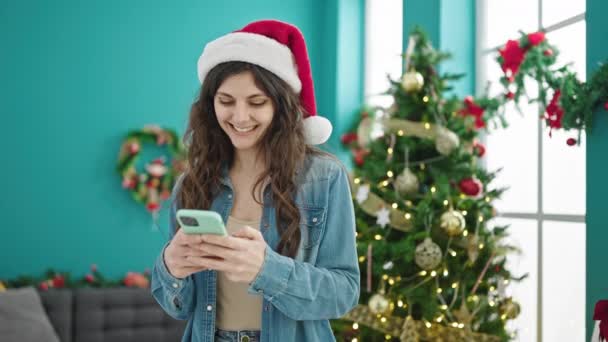 Joven mujer hispana hermosa usando teléfono inteligente celebrando la Navidad en casa - Metraje, vídeo
