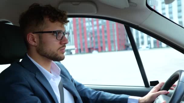 A férfi kényelmesen ül a vezetőülésen a kocsijában. Üzletember biztonsági övvel vezetés közben. Közlekedés, üzlet és ember koncepció. Lassú mozgás. - Felvétel, videó
