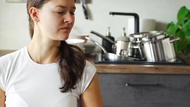 Mladá žena sedí a medituje na pozadí špinavého nádobí v kuchyni. Zpomal, sebedůvěra, pomalý život. Vysoce kvalitní 4K záběry - Záběry, video