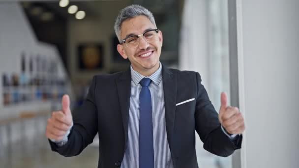 若いヒスパニックの男のビジネスワーカーは,オフィスで親指でジェスチャーをする自信を持って微笑みます - 映像、動画