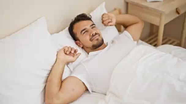Young hispanic man waking up stretching arms at bedroom - Metraje, vídeo