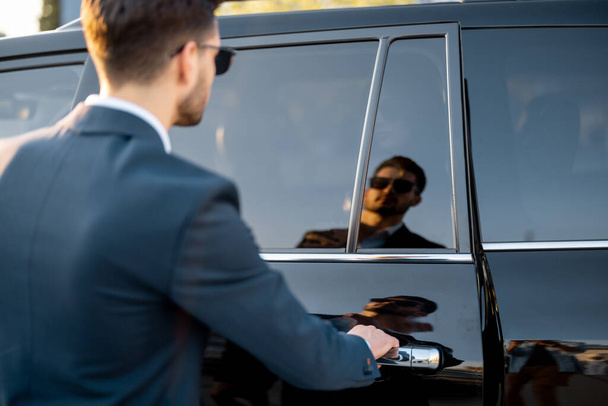 Portré egy üzletemberről, aki kinyitja a jármű ajtaját, tükröződés az autóban - Fotó, kép