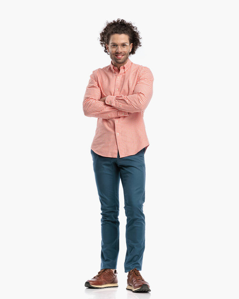 full body picture of smart casual man with curly hair and glasses smiling and crossing arms while standing in front of white background - Foto, Imagem