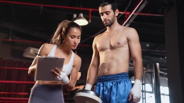 Азиатка Муай Тай боксер и личный тренер по боксу, глядя на физический прогресс в тренажерном зале отражающий приверженность росту мышц тела и боксу производительности. Импет - Кадры, видео