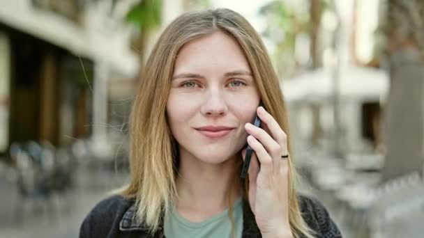 Jovem loira sorrindo confiante falando no smartphone na rua - Filmagem, Vídeo