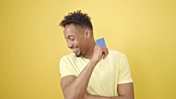 Africano americano apontando para cartão de crédito fazendo polegar acima gesto sobre fundo amarelo isolado - Filmagem, Vídeo