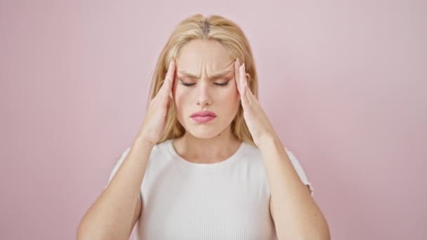 Mladá blondýna žena trpí bolestí hlavy přes izolované růžové pozadí - Záběry, video