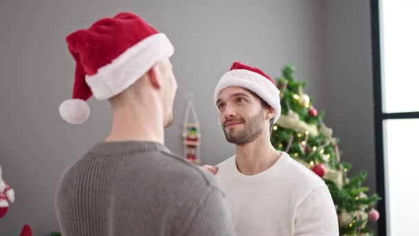 Двое мужчин празднуют Рождество целуясь дома - Кадры, видео