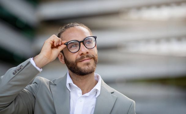 Jóképű fiatal üzletember Stílusos szemüveg áll a szabadban a City Street, és néz félre, Closeup portré boldog Y-generációs férfi vállalkozó öltönyben pózol kívül Office Center - Fotó, kép