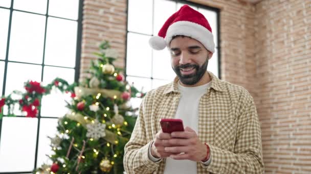 Jeune homme hispanique célébrant Noël en utilisant un smartphone à la maison - Séquence, vidéo