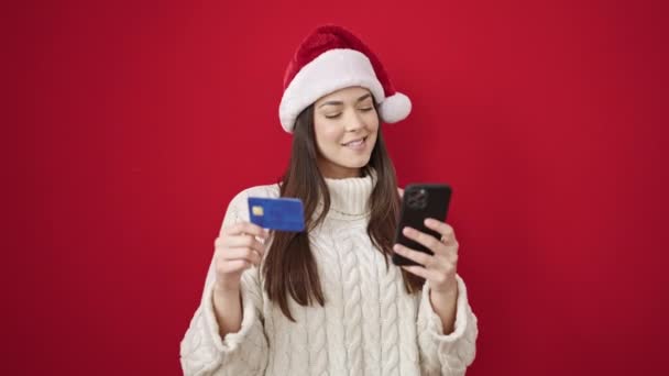 Νέα όμορφη ισπανόφωνη γυναίκα κάνει Χριστούγεννα online ψώνια με smartphone πάνω από απομονωμένο κόκκινο φόντο - Πλάνα, βίντεο