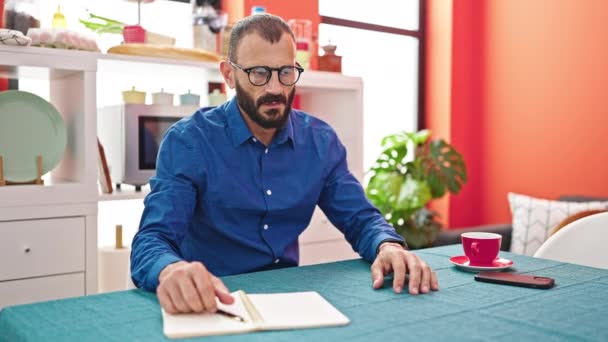 A fiatal spanyol férfi jegyzetfüzetre ír, stresszes az ebédlőben. - Felvétel, videó