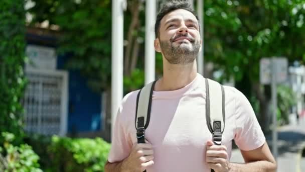 Junger hispanischer Tourist mit Rucksack sieht sich lächelnd im Park um - Filmmaterial, Video