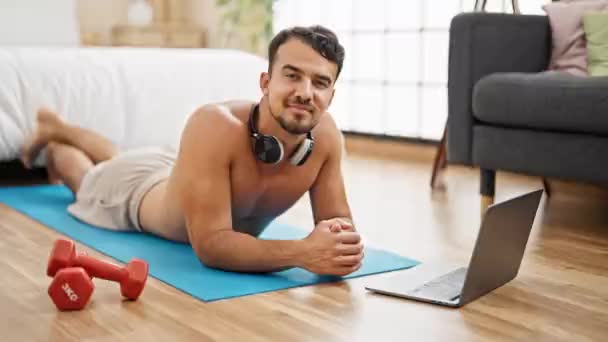 Jeune homme hispanique souriant confiant couché sur le tapis de yoga dans la chambre - Séquence, vidéo