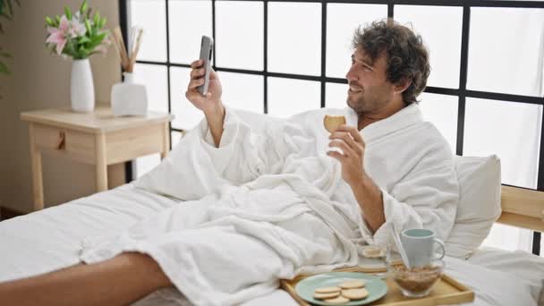 Giovane uomo ispanico che fa colazione facendo videochiamata in camera da letto - Filmati, video