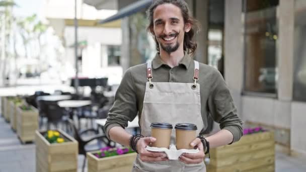 Fiatal spanyol férfi pincér mosolyog magabiztos gazdaság elvinni a kávét a kávézó teraszán - Felvétel, videó