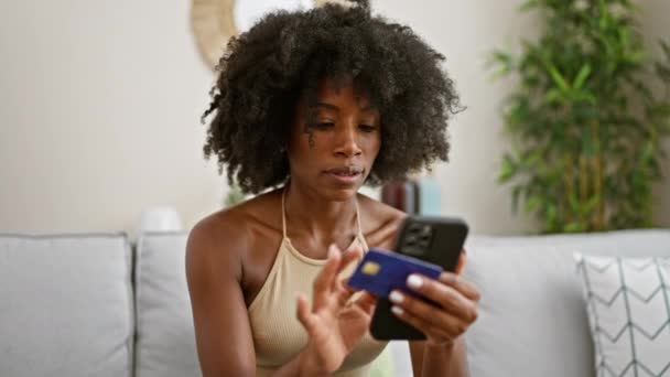 Afričanky americká žena nakupování s smartphonem a kreditní kartou sedí na pohovce doma - Záběry, video