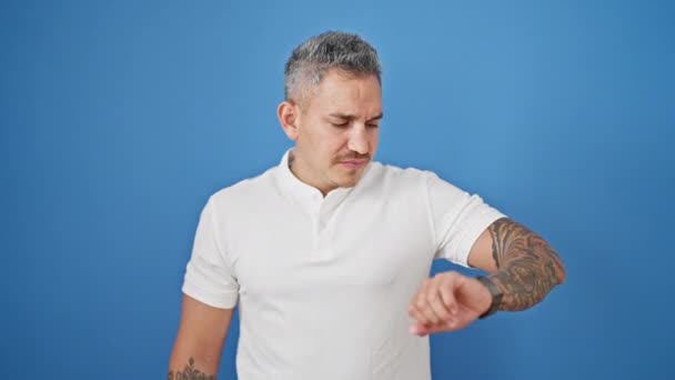 Jeune homme hispanique regardant montre stressée sur fond bleu isolé - Séquence, vidéo