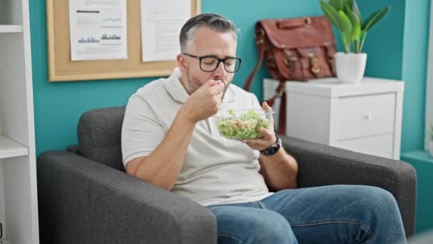 Grijsharige zakenman op zoek naar horloge etende salade op kantoor - Video