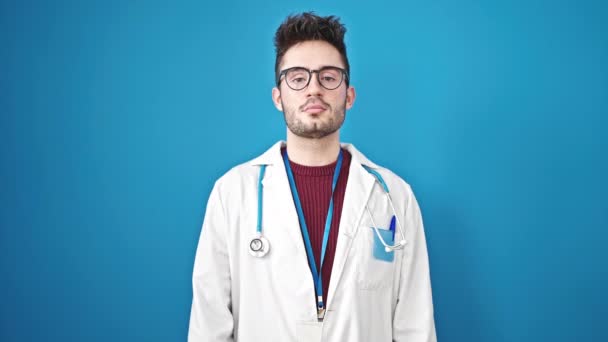 Junger hispanischer Arzt leistet einen Eid mit der Hand auf der Brust vor isoliertem blauem Hintergrund - Filmmaterial, Video