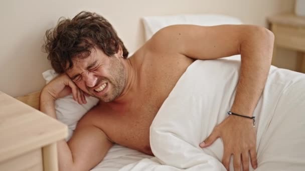 Jonge Spaanse man lijdt aan buikpijn liggend op bed shirtloos in de slaapkamer - Video