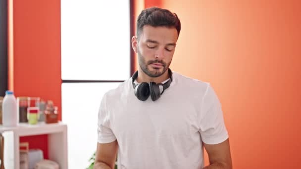 Fiatal spanyol férfi okostelefont visel fejhallgató áll az ebédlőben - Felvétel, videó