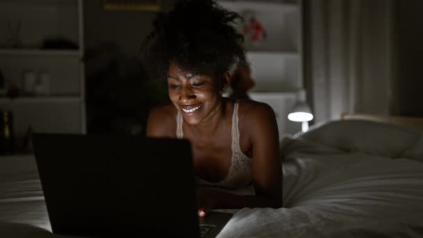 Africano americano mulher vestindo lingerie usando laptop deitado na cama no quarto - Filmagem, Vídeo