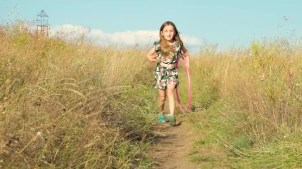 Una niña corre a través de un campo de verano con un aro de gimnasia en la mano. - Imágenes, Vídeo