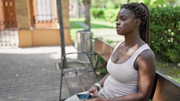 Αφροαμερικανή γυναίκα που χρησιμοποιεί smartphone με σοβαρή έκφραση στο πάρκο - Πλάνα, βίντεο