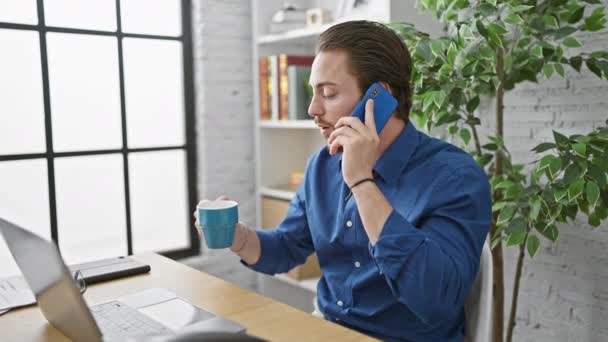 Młody latynoski pracownik biznesowy rozmawiający przez smartfona pijący kawę w biurze - Materiał filmowy, wideo