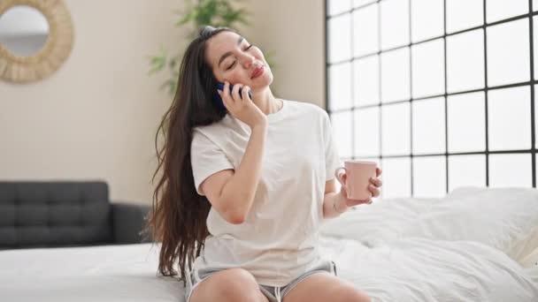 Joven hermosa mujer hispana hablando en smartphone bebiendo café en el dormitorio - Imágenes, Vídeo