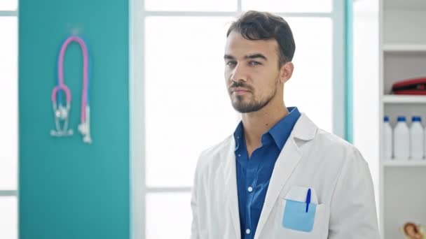 Młody latynoski lekarz stojący z poważnym wyrazem twarzy noszący stetoskop w klinice - Materiał filmowy, wideo