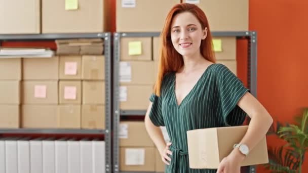 Jeune rousse femme commerce électronique entreprise travailleur tenant paquet souriant au bureau - Séquence, vidéo