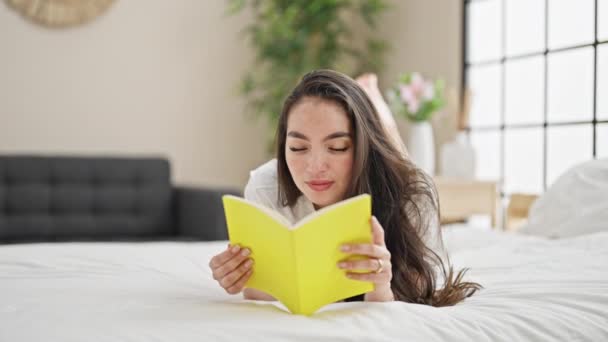 Νεαρή όμορφη ισπανόφωνη γυναίκα διαβάζει βιβλίο ξαπλωμένη στο κρεβάτι στο υπνοδωμάτιο - Πλάνα, βίντεο