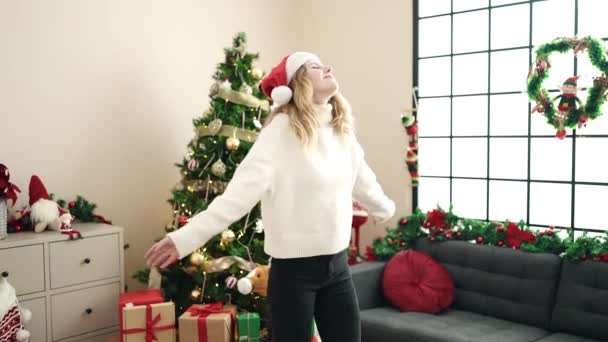 Junge blonde Frau lächelt selbstbewusst, wenn sie zu Hause am Weihnachtsbaum steht - Filmmaterial, Video