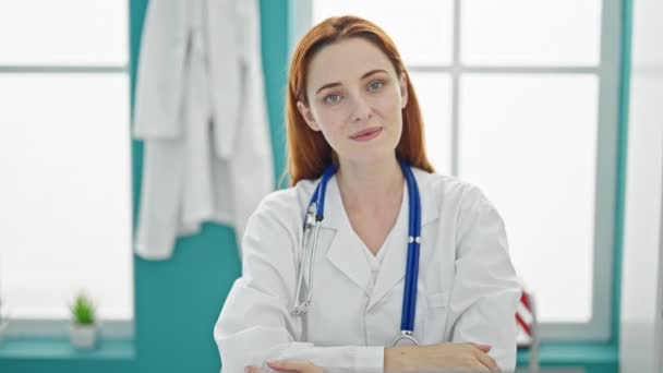 Joven pelirroja doctora haciendo pulgar hacia arriba sonriendo en la clínica - Imágenes, Vídeo