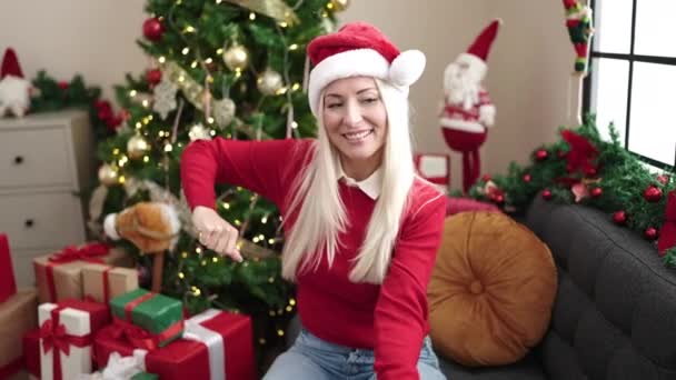 Fiatal szőke nő ül kanapén karácsonyfa tánc otthon - Felvétel, videó