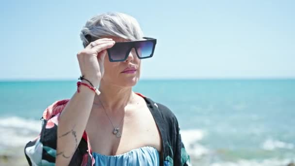 Młoda kobieta turystka w bikini i okularach słonecznych uśmiechnięta na plaży - Materiał filmowy, wideo