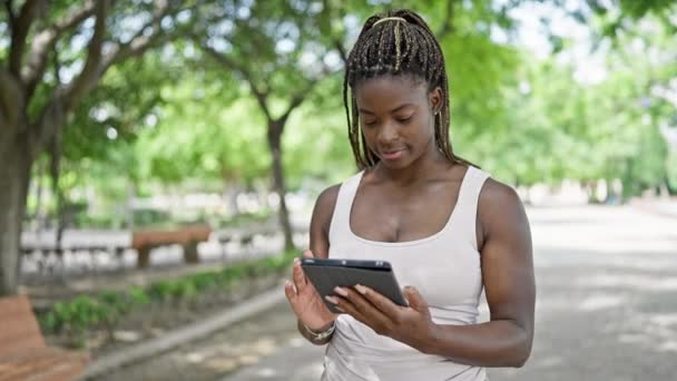 donna afroamericana sorridente fiducioso utilizzando touchpad al parco - Filmati, video