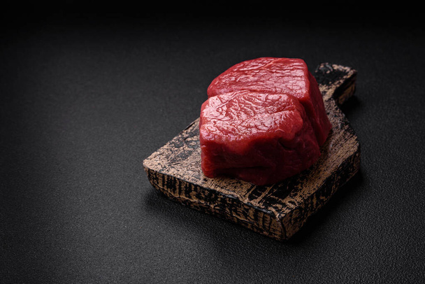 Roh-Filetsteak Mignon-Rindfleisch mit Salz, Gewürzen und Kräutern auf dunklem Betongrund - Foto, Bild