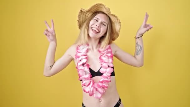 Fiatal szőke nő turista visel bikini és hawaii lei csinál győzelem gesztus felett elszigetelt sárga háttér - Felvétel, videó