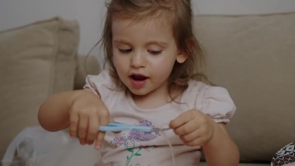 Menina bebê fio de corte com tesoura necessária para costurar enquanto está de pé no sofá. Artefactos de malha. - Filmagem, Vídeo